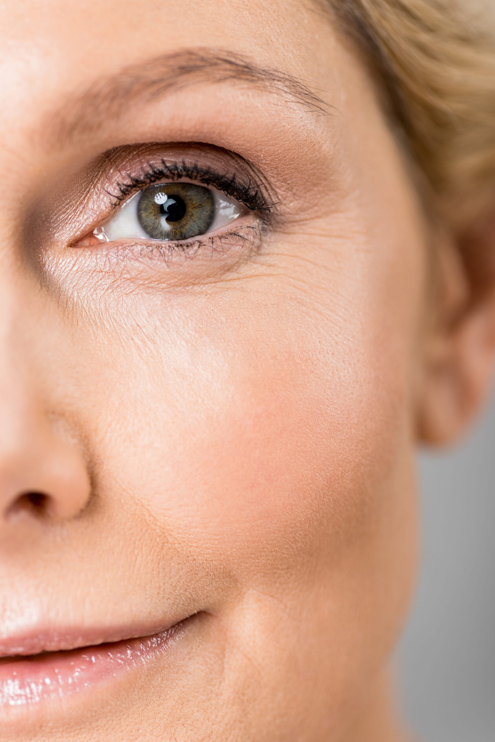 Selective focus of attractive and mature woman looking at camera isolated on grey